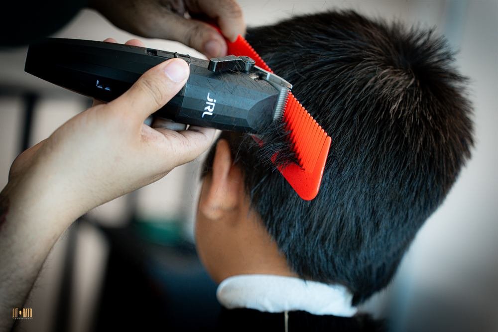 Barber using a clipper over a comb on the back of a client's head